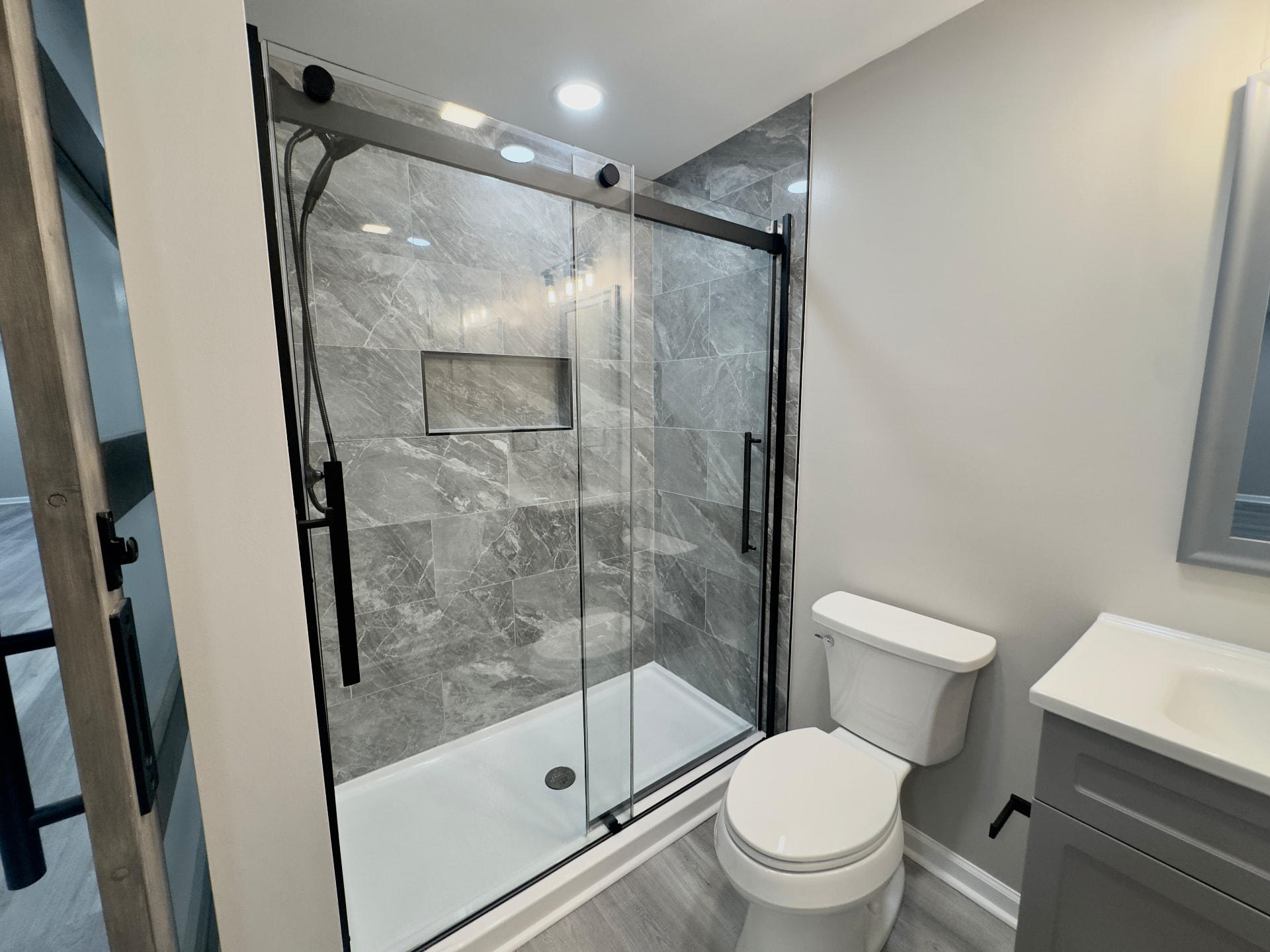 Walk-in shower with marble-look tile, built-in niche, and black glass door hardware
