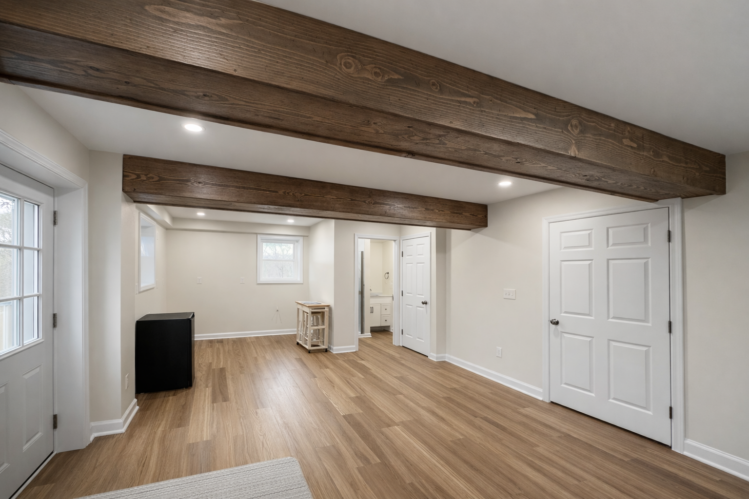 Finished basement with wood-look flooring and exposed dark wood ceiling beams